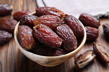 Many tasty dried dates in bowl on wooden table, closeup