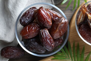 Many tasty dried dates in bowls and leaves on table, flat lay