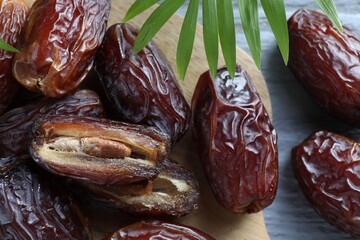 Many tasty dried dates and leaf on blue table, top view