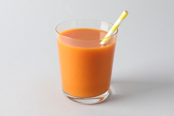 Fresh carrot smoothie in glass on light grey background, closeup