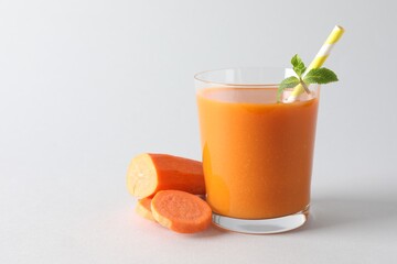Fresh carrot smoothie in glass and cut vegetable on light grey background, closeup. Space for text