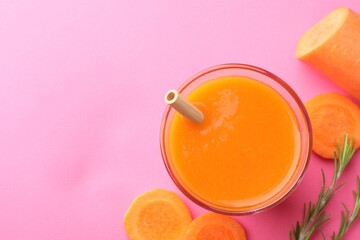 Fresh carrot smoothie in glass, rosemary and cut vegetable on pink background, flat lay. Space for...