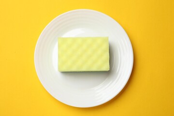 Plate with sponge on yellow background, top view