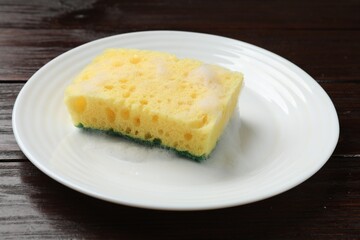 Yellow sponge with foam and plate on wooden table, closeup