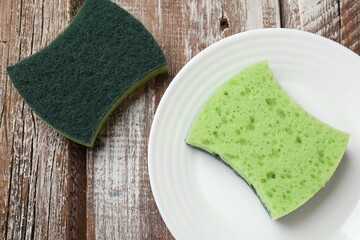 Green sponges and plate on wooden table, flat lay