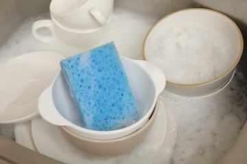 Blue sponge, dishes and foam in sink, closeup