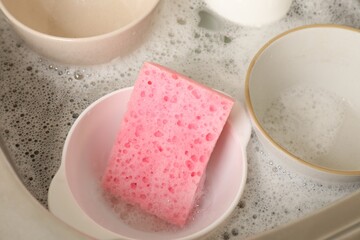 Pink sponge, dishes and foam in sink, closeup
