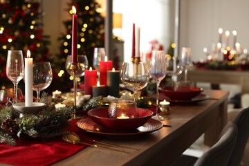 Christmas table setting with stylish dishware, glasses and burning candles in festive decorated room