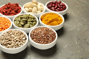 Different superfoods in bowls on grey table, closeup