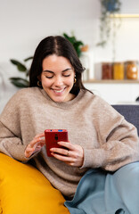 Vertical shot of young happy teenage girl using mobile phone while relaxing on sofa at home