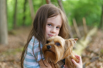 Little girl hugging a small dog in a summer forest. Concept of friendship between a child and an...