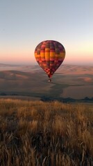Fototapeta premium A colorful hot air balloon floats over rolling hills at sunrise, showcasing serene landscapes.
