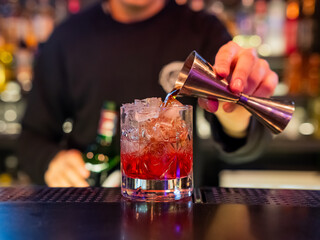 The bartender pours a red cocktail. 