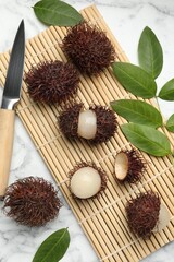 Delicious ripe rambutans, knife and green leaves on white marble table, flat lay