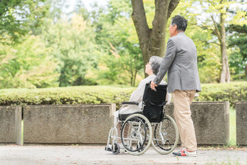 車椅子で公園を散歩するシニア・高齢者夫婦（介護）
