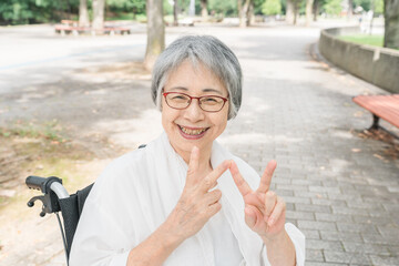 公園で散歩中・気分転換中にピースサインをする優しい笑顔のシニア女性
