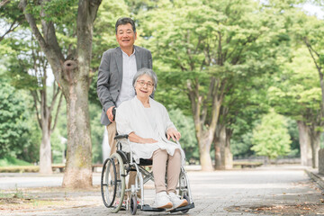 車椅子で公園を散歩するシニア・高齢者夫婦（介護）
