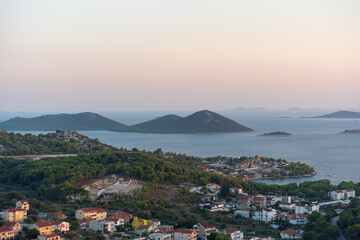 Scenic coastal town with lush green hills and calm blue sea during peaceful sunset. Concept of...
