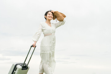 スーツケースを持って旅行に来た若いアジア人女性(自由・開放・夏・リゾート・バカンス)
