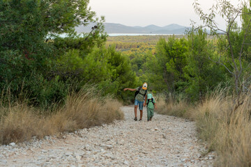 Two brothers hiking in nature on rocky path surrounded by lush greenery and scenic hills. Concept of outdoor adventure, bonding, and active lifestyle for kids.