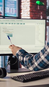 Programmer at desk types code into computer, developing software programs, entering commands. Man at home fixing errors in application, implementing new features pointing to code with pen, camera A
