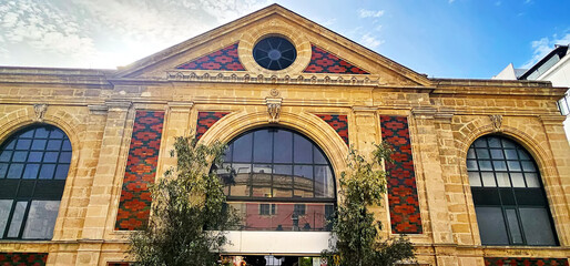 Jerez de la Frontera; facade of a historic building with arched windows and triangular pediment; red and black patterned details; trees in the foreground;