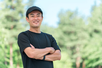 Fototapeta premium 新緑の公園でスポーツウェアを着て腕組みをするアジア人男性 