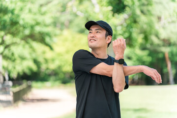 新緑の公園でストレッチをするスポーツウェア姿のアジア人男性
