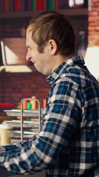 Man in home office stretches back while looking at UI on PC screen, feeling fatigued while executing programming code. IT developer feeling backpain, relieving pain, writing and testing code, camera B
