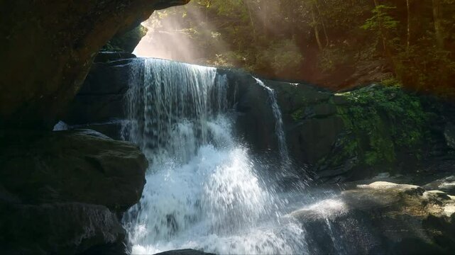 Slow motion shot of Little Bradley Falls, a waterfall in the forest of North Carolina, with sunbeams shining through the foliage