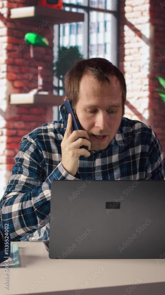 Poster manager in home office sitting at desk in front of laptop, calling employee to confront him about mi