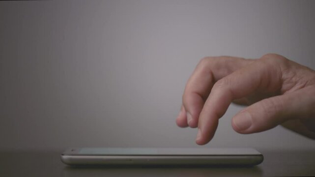 Close-up side view of a person thinking before sending, writing a message or email on the smartphone on a table on a neutral background