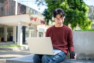 Smiling man freelancer in wireless headphone working remotely in a sunny urban park.