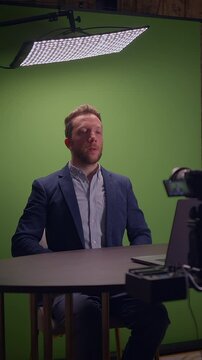 A man in a suit uses a laptop in front of a green screen, perfect for video production