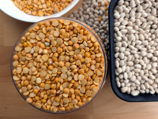 White beans in a black container and small, yellow, split peas in a clear container and white bowl