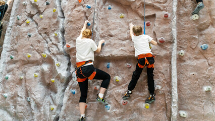 Mother and son climb up with a belay on a climbing wall