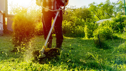 gardener with grass trimmer mows lawn or grass. selective focus