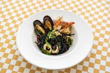 squid Ink spaghetti spicy seafood or stir fried black pasta with shrimp mussels squid peppercorns and holy basil leaves in white plate or dish on yellow brown table for Italian cuisine with Thai food