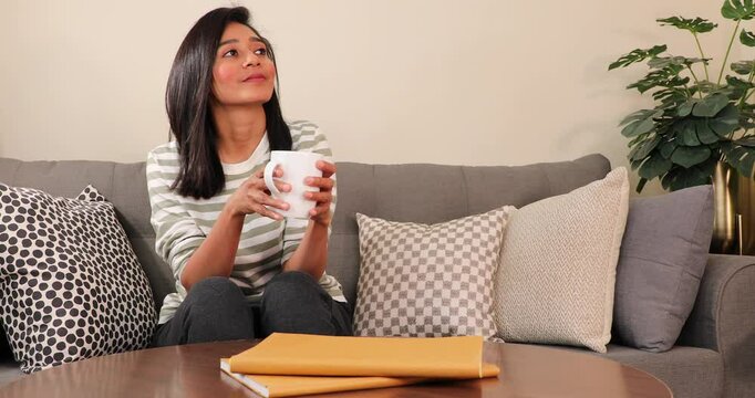 Young Indian women staying on couch and holgding a meg of coffee