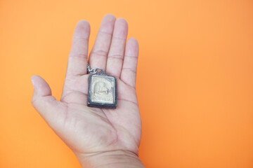 Hand holds Buddha amulet. Orange background. Concept, faith and belief of Buddhist for holy to...