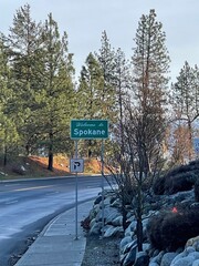 Welcome to Spokane road sign - Pine trees are visible in the background.