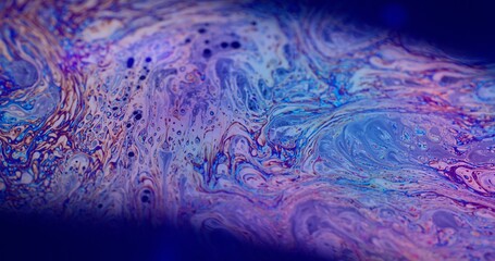 Psychedelic fantasy. Dye mixing. Defocused multicolor purple green liquid paint curve acrylic slick on dark black blurred light abstract art background.