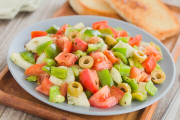 Fresh vegan salad of tomato, olive, green pepper and cucumber, seasoned with oregano, salt, black pepper and olive oil, served on blue plate (Selective Focus, Focus in the middle of the image)