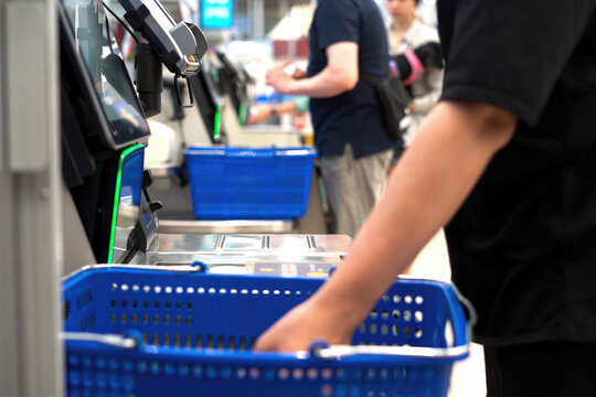 Customer uses an automated self-checkout kiosk to scan groceries, close-up.