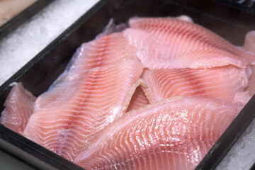 A fresh tilapia fish fillet lies on an icy counter in a store under a cooling spray