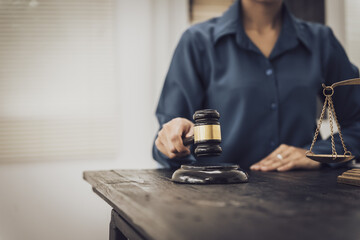 Close-up of an Asian female lawyer sitting at her desk in a law office. A wooden hammer and brass scales symbolize justice. She demonstrates expertise in the legal and justice process