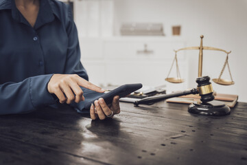 Close-up of an Asian female lawyer sitting at her desk in a law office. A wooden hammer and brass scales symbolize justice. She demonstrates expertise in the legal and justice process