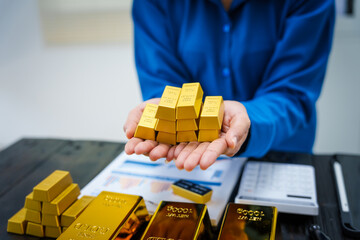 An Asian businesswoman sits at her desk analyzing gold bar prices, buying and selling gold, trading...
