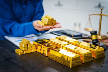 An Asian businesswoman sits at her desk analyzing gold bar prices, buying and selling gold, trading...