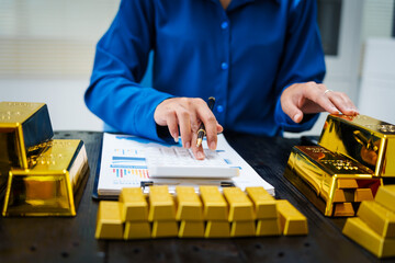 An Asian businesswoman sits at her desk analyzing gold bar prices, buying and selling gold, trading...